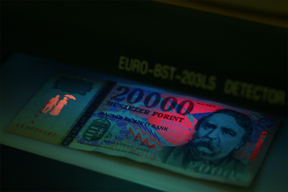 UV-C fényben: a hamis pénz festett vízjele reagál, az igazi pénz vízjele pedig nem (mivel nem festék hozza létre a képet, hanem a papírban a rostsűrűség változása)