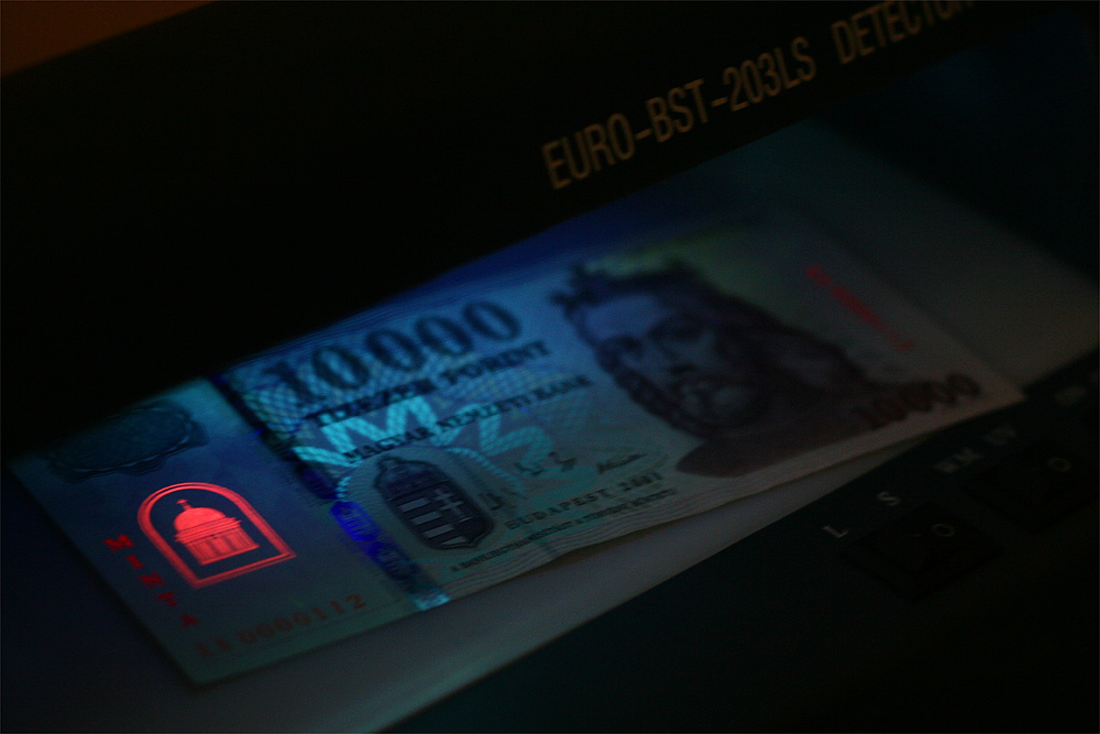 UV-C fényben: a hamis pénz festett vízjele reagál, az igazi pénz vízjele pedig nem (mivel nem festék hozza létre a képet, hanem a papírban a rostsűrűség változása)