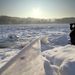 Egy férfi figyeli távcsővel a befagyott Oder folyó jegét Németországban.