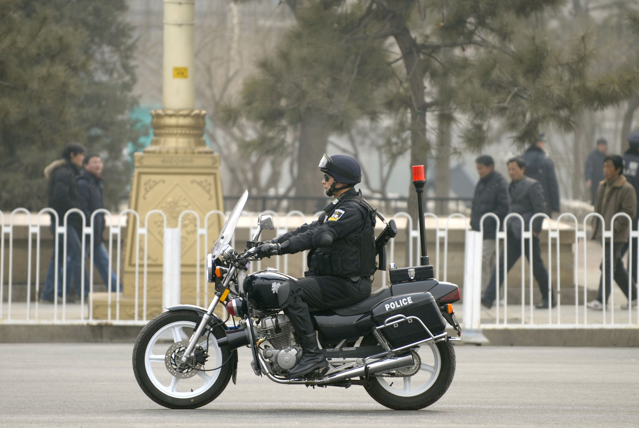 Délnyugat-kínai etnikai kisebbségek népviseletébe öltözött hoszteszekkel fényképezkedik egy rendőr a Tienanmen téren.