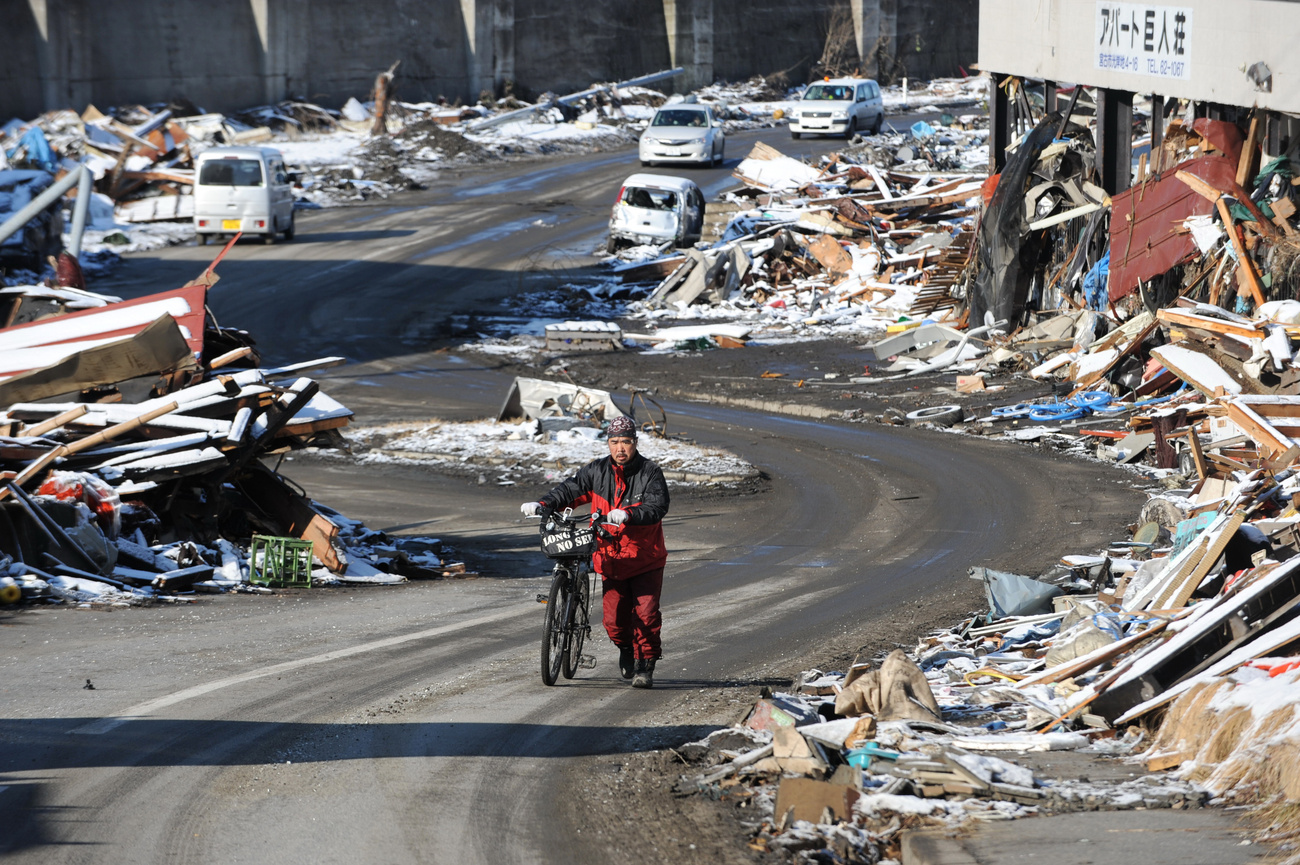 A romok között tolja biciklijét egy férfi Mijako városban