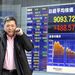Üzletember telefonál egy részvényárfolyamokat jelző tábla mellett Tokióban