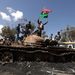 Felkelők lengetik a líbiai zászlót Kadhafi hadseregének kilőtt tankján