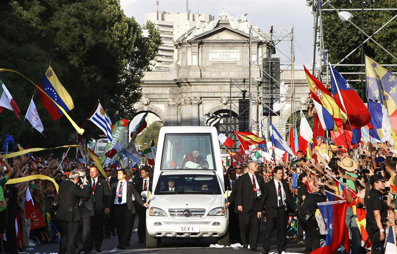 Pápaellenes tüntetők maroknyi csoportja és rendőrségi járművek a Puerta del Sol téren