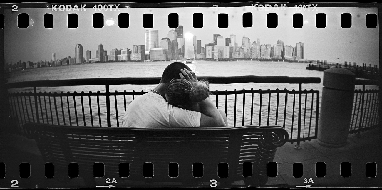 Egy ölelkező pár figyeli az újjáépülő Manhattant a Hudson-folyó partján pihenve.