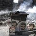 A portrékon a szíriai elnök bátyja és apja,  mögöttük gomolygó füst és a romokban heverő város.