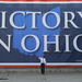 Mitt Romney egy győzelmét hirdető óriásplakát előtt Ohióban, amely azonban a felmérések szerint inkább Obama felé húzhat.