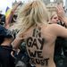 A nagy, fekete betűkkel, a meztelen hátukra írt In Gay We Trust (Mi a melegekben hiszünk) jelszót kiabálta a Femen mozgalom négy aktivistája. 