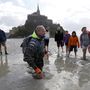 Árapály-turisták és térdig a tengeriszapba süllyedő vezetőjük Mont Saint-Michelnél.
