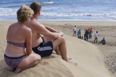 Egy pár sétál a naplementében egy lepelbe csavart menekült holtteste előtt a spanyol Fuerteventura tengerparton.