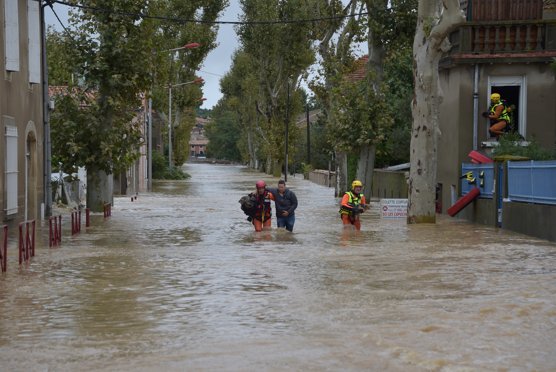 A lakosok kimenekítését végző francia tűzoltók egyike egy kisfiút visz árvízben álló utcán gyalogolva a dél-franciaországi Trebes városban 2018. október 15-én