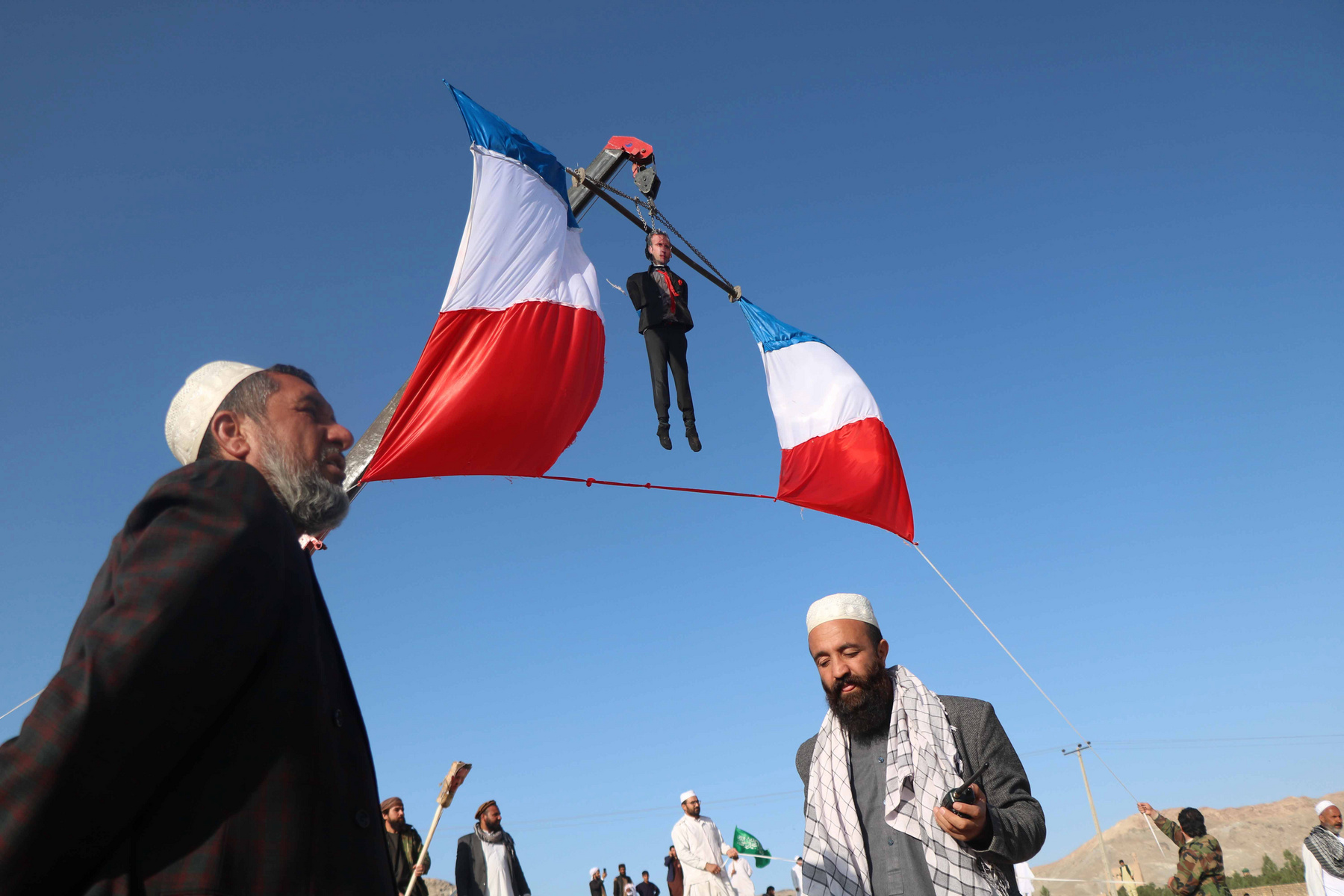 Tüntetõk Emmanuel Macron gúnyfiguráját lógatják egy daruról a francia elnök Mohamed prófétát ábrázoló karikatúrákkal és az iszlámmal kapcsolatos kijelentései miatt tartott tiltakozáson a nyugat-afganisztáni Herátban 2020. október 30-án. 