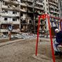 Egy gyerek ül a hintán Kijevben, egy megrongálódott épület előtt 2022. február 25-én