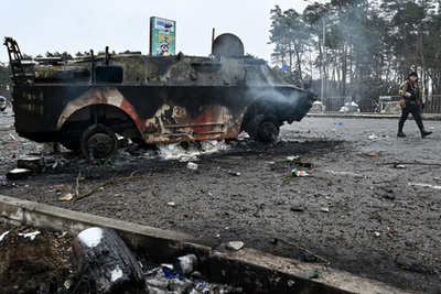 Fegyveres férfi sétál egy kiégett katonai jármű mellett a Kijevhez közeli Brovai városában 2022. március 1-jén