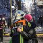 Egy helyszínen dolgozó tűzoltó megölel egy nőt Kijevben egy robbanás által megsérült lakóház előtt 2022. március 15-én