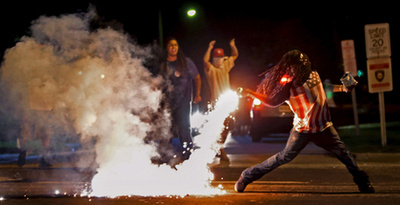 Könnygázgránátot dob vissza  rendőröknek egy tüntető Fergusonban.