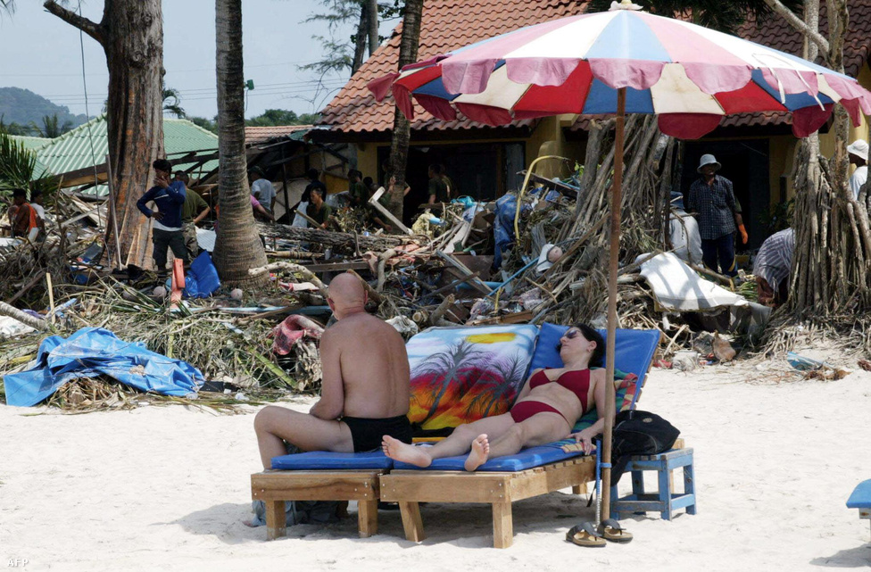 Turisták napoznak hat nappal a katasztrófa után Phuket szigetén, miközben a háttérben még takarítják el a törmeléket a parton. Tíz évvel a pusztító cunami után már sok partmenti város és halászfalu újjáépült, a túlélők pedig új életet kezdtek.