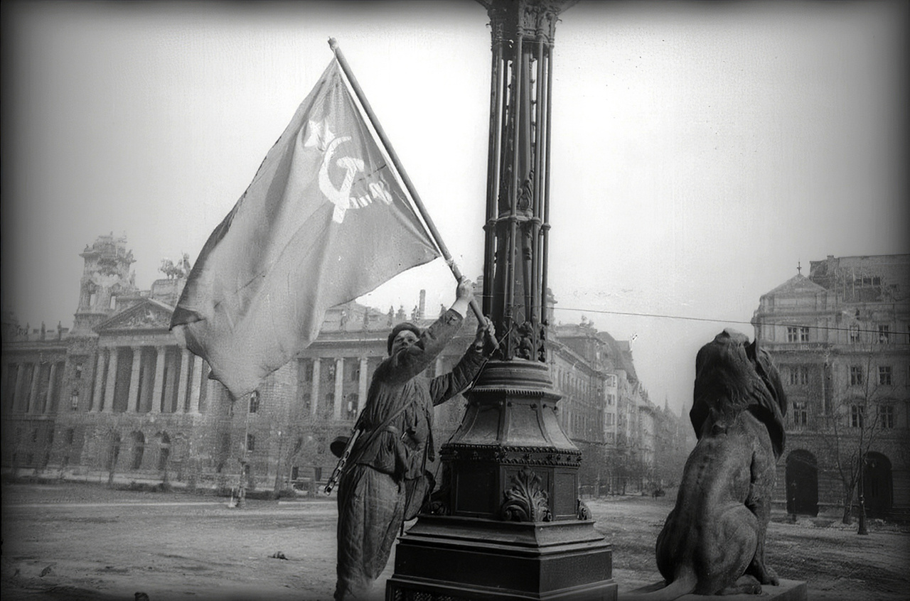 Szovjet vörös zászló lobog a pesti New York palota tetején. A kép erősen emlékeztet Haldej leghíresebb fotójára, a Berlin bevételét a Reichstag tetején szovjet zászlót kitűző győzedelmes vörös katonával hitelesítő propagandaképre. Az a kép Haldej sok más felvételéhez hasonlóan erősen manipulált: a valós események után egy nappal a fénykép kedvéért játszatta újra a történteket, a fotós maga varrta hozzá a zászlót, a montírozások után pedig kiretusált a katona karjáról egy második karórát, hogy mégse legyen ott a zabrálások egyértelmű jele. A válogatásunkban látható képek elsősorban szintén a propagandáról szóltak. Többségüket feltehetően valóban Haldej készítette, de biztosra ezt nem lehet venni mindegyik esetben.
