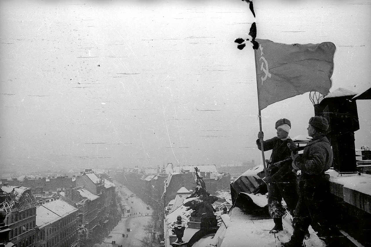 Szovjet vörös zászló lobog a pesti New York palota tetején. A kép erősen emlékeztet Haldej leghíresebb fotójára, a Berlin bevételét a Reichstag tetején szovjet zászlót kitűző győzedelmes vörös katonával hitelesítő propagandaképre. Az a kép Haldej sok más felvételéhez hasonlóan erősen manipulált: a valós események után egy nappal a fénykép kedvéért játszatta újra a történteket, a fotós maga varrta hozzá a zászlót, a montírozások után pedig kiretusált a katona karjáról egy második karórát, hogy mégse legyen ott a zabrálások egyértelmű jele. A válogatásunkban látható képek elsősorban szintén a propagandáról szóltak. Többségüket feltehetően valóban Haldej készítette, de biztosra ezt nem lehet venni mindegyik esetben.